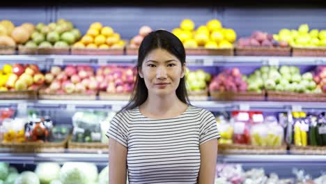 Retrato-De-Una-Atractiva-Joven-Asiática-Parada-En-Un-Supermercado-Con-Estantes-De-Frutas-En-El-Fondo,-Mirando-La-Cámara-Y-Sonriendo.-Concepto-De-Negocio-Y-Personas-De-Comercio