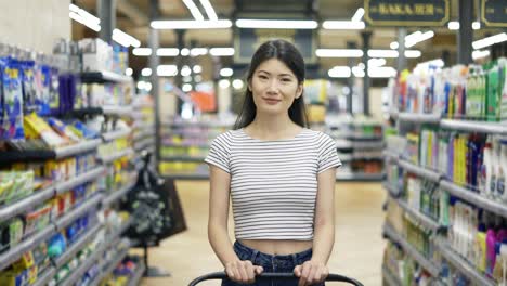 Happy-Asian-girl-walks-around-the-supermarket-with-a-shopping-cart-and-looking-at-the-camera.-Shopping-trip.-daily-business