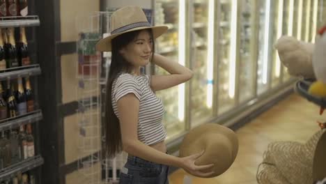 and-Asian-girl-shopper-trying-on-hats-in-a-store.-Shopping.-pastime-style