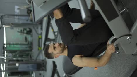 Vídeo-Vertical-De-Un-Hombre-Musculoso-Realiza-Ejercicios-En-Un-Aparato-De-Entrenamiento-Deportivo-Para-Los-Músculos-De-Las-Piernas,-Levantando-Pesas