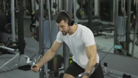 Bodybuilder-Typ-Im-Fitnessstudio,-Der-Die-Hände-In-Kopfhörern-Von-Den-Seiten-Hochpumpt