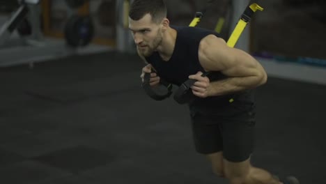 Sportsman-doing-confrontation-running-exercise-with-TRX-straps-at-gym