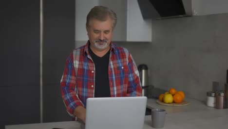 Bärtiger-Alter-Mann-Benutzt-Laptop-In-Der-Küche