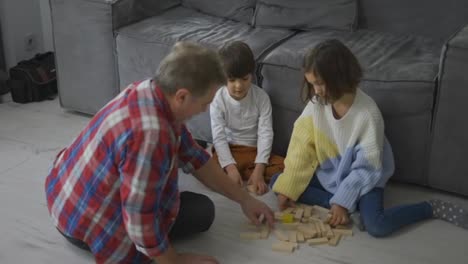Glückliche-Kinder,-Die-Mit-Opa-Auf-Dem-Boden-Holzbauer-Spielen