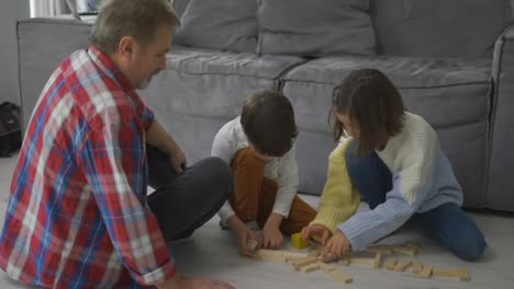 Happy-children-playing-wooden-constructor-on-the-floor-with-grandad,-slow-motion