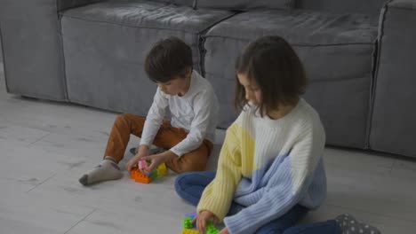 Busy-little-children-boy-girl-siblings-friends-play-brick-toy-constructor-on-floor