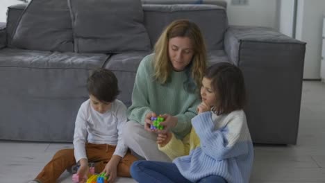 Happy-young-adult-mother-playing-with-two-cute-small-kids,-having-fun-sit-on-floor
