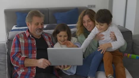 Glückliche-Familiengenerationen,-Großvater-Mit-Zwei-Enkelkindern-Und-Tochter-Sitzen-Auf-Dem-Sofa-Mit-Laptop