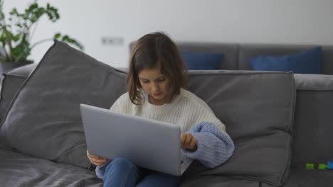 Kleines-Schulmädchen-Benutzt-Einen-Laptop-Computer,-Der-Auf-Dem-Sofa-Sitzt