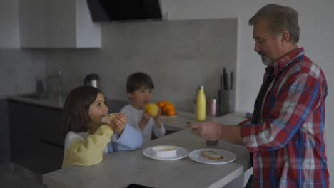 Two-small-children-are-eating-sandwiches-made-by-grandfather,-slow-motion