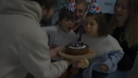 Little-brother-and-sister-blows-out-the-candles-on-cake-together-in-a-circle-of-happy-family