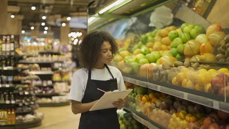 Portrait-of-african-american-female-staff-person-standing-in-front-of-the-fruit-shelves-with-tablet