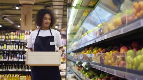 Pretty-multiracial-worker-in-black-apron-stocking-the-fruits-in-supermarket