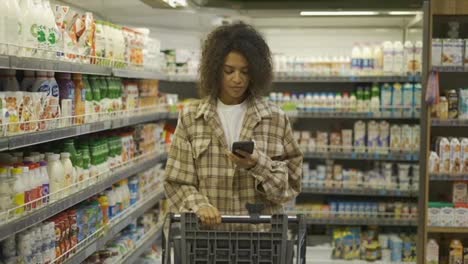 African-American-with-shopping-cart-using-smartphone-at-supermarket