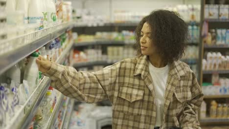 Black-woman-doing-grocery-shopping-in-supermarket,-looking-at-full-shelves-buying-food
