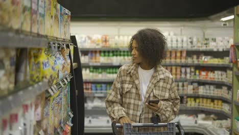 African-American-with-shopping-cart-using-smartphone-at-supermarket,-slow-motion