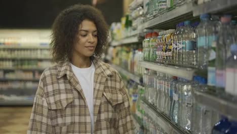 Black-woman-doing-grocery-shopping-in-supermarket,-taking-water-bottle-from-the-shelf