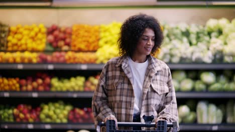 Cheerful-woman-walks-through-supermarket-with-cart,-taking-a-pack-of-potatoes