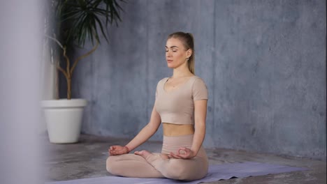 Attractive-caucasian-woman-sitting-in-lotus-pose-or-Padmasana-with-closed-eyes,-holding-her-hands-in-Gyan-Mudra