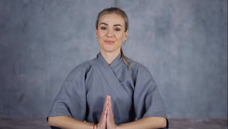 Smiling-female-coach-yoga-in-robe-makes-Namaste-gesture-by-hands