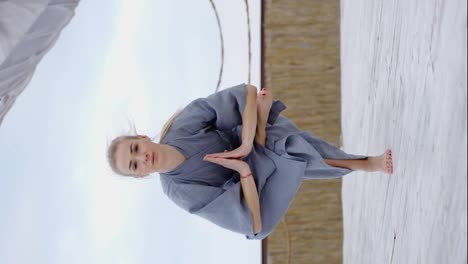 Attractive-blonde-woman-in-robe-doing-yoga-Eka-Pada-Utkatasana-outdoors