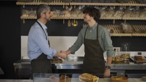Close-up-portrait-of-happy-successful-family-business-owners-handshaking-in-their-bakery-store-looking-at-camera-and-smiling.-Father-and-son