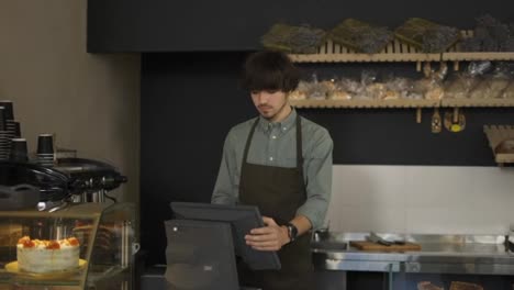 Young-cashier-in-apron-typing-on-touch-screen-in-bakery-store.-Close-up,-indoor,-slow-motion