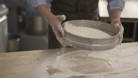 Hands-holding-sieve-and-sifting-flour-at-the-kithen.-Close-up,-indoor,-slow-motion