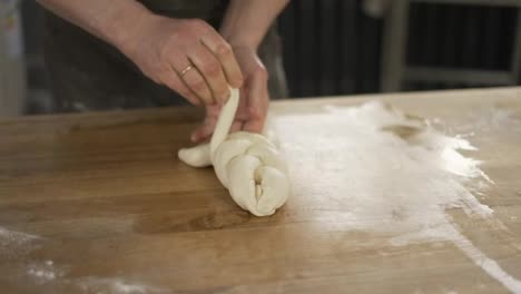 Baker-kneads-dough-and-making-bread.-Chef-weaves-a-pigtail-from-dough-on-table.-Baker-hands-close-up.-Preparing-bread.-Male-hands-close-up