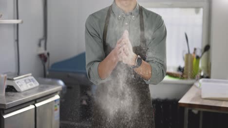 Handsome-male-baker-claps-and-scatters-white-flour-in-the-air.-Young-man-making-homemade-bread-claps-with-a-handful-of-organic