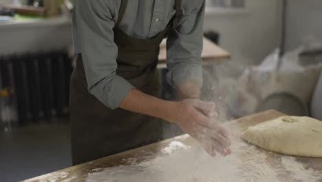 Unrecognizable-male-baker-claps-and-scatters-white-flour-in-the-air.-Young-man-making-homemade-bread-claps-with-a-handful-of-organic-whole-wheat-flour-in-each-hand.-Slow-motion,-close-up
