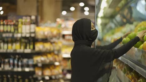 Muslim-women-shopping-for-groceries,-taking-fruits-from-the-shelf,-side-view