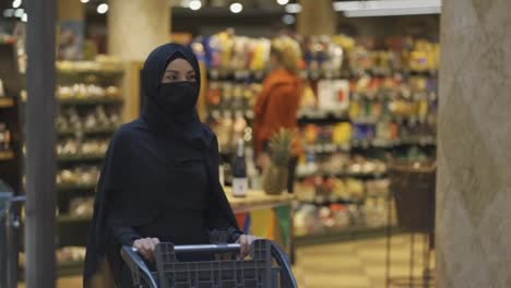 Moderne-Muslimische-Frau-Im-Hijab,-Die-Im-Supermarkt-Lebensmittel-Einkauft-Und-Produkte-Auswählt,-Mit-Maske