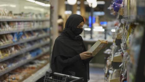Mujer-Con-Hiyab-Y-Máscara-Protectora-Haciendo-Compras-En-El-Supermercado,-Eligiendo-Copos-De-Maíz