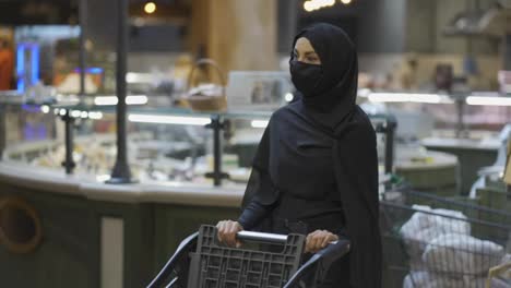 Frau-Im-Hijab-Und-Schutzmaske-Beim-Einkaufen,-Einkaufswagen-Schieben