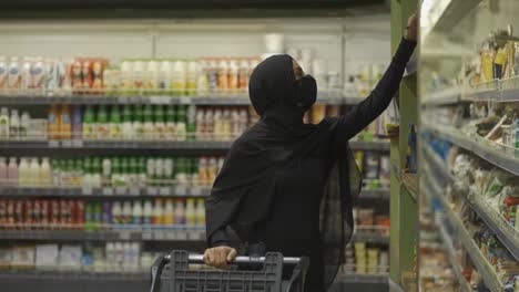 Woman-in-hijab-and-protective-mask-doing-shopping,-takes-product-from-the-shelf,-slow-motion