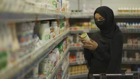 Woman-in-hijab-and-protective-mask-doing-shopping,-takes-product-from-the-shelf-in-a-milk-section