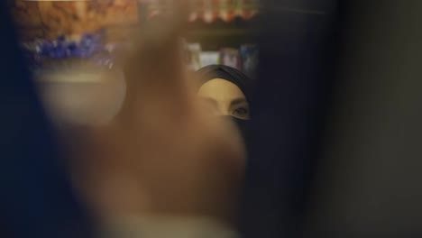 Woman-in-hijab-and-mask-takes-product-from-the-shelf,-footage-from-inside