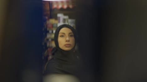 Woman-in-hijab-takes-product-from-the-shelf,-footage-from-inside