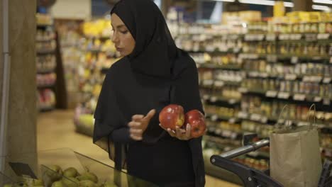 Mujer-Musulmana-Comprando-Comestibles,-Tomando-Manzanas-Rojas-Del-Pasillo-De-Frutas