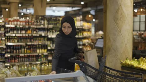 Muslim-woman-shopping-for-groceries,-taking-some-berries-from-the-fruit-aisle