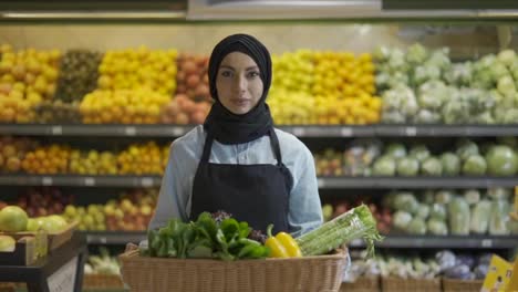 Portrait-of-a-woman-in-hijab-standing-with-basket-of-fresh-vegetables-in-the-supermarket