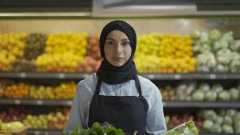 Portrait-of-a-woman-in-hijab-standing-with-basket-of-fresh-vegetables-and-greens-in-the-supermarket