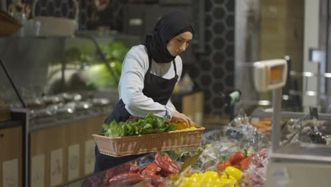 Muslimische-Frau-In-Schürze-Füllt-Das-Frische-Gemüse-Im-Supermarkt-Nach