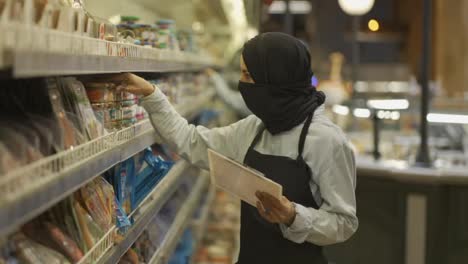 Mujer-Con-Bufanda-Negra-Trabajando-En-La-Tienda,-Inspeccionando-Estantes-Con-Tableta