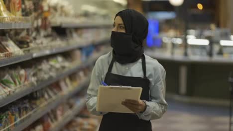 Woman-in-black-scarf-working-in-store,-inspecting-shelves-with-tablet,-slow-motion