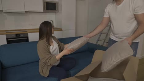 Married-couple-with-pregnant-wife-in-the-living-room,-unpacking-pillow-from-the-box