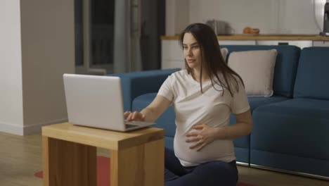 A-pregnant-woman-in-home-clothes-is-sitting-on-the-floor-and-using-a-laptop