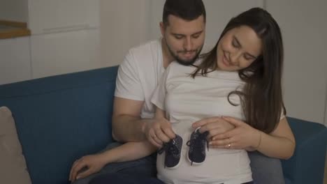 Beautiful-pregnant-woman-and-her-husband-holding-baby-shoes-on-belly