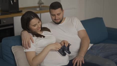 Portrait-of-pregnant-woman-and-her-husband-holding-baby-shoes-on-belly